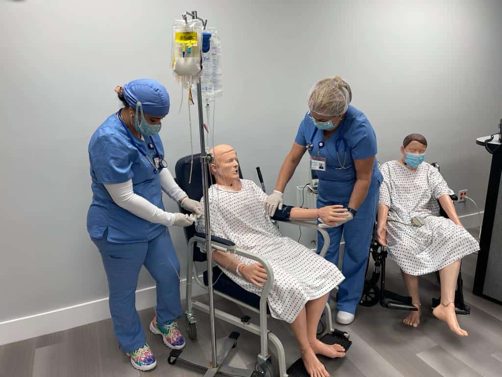 FVI Miami patient care tech program students practicing hands-on skills with a patient simulator in a wheelchair