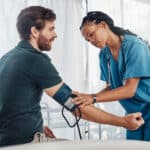 Miami patient care tech program graduate working in hospital - Nurse and man with blood pressure test