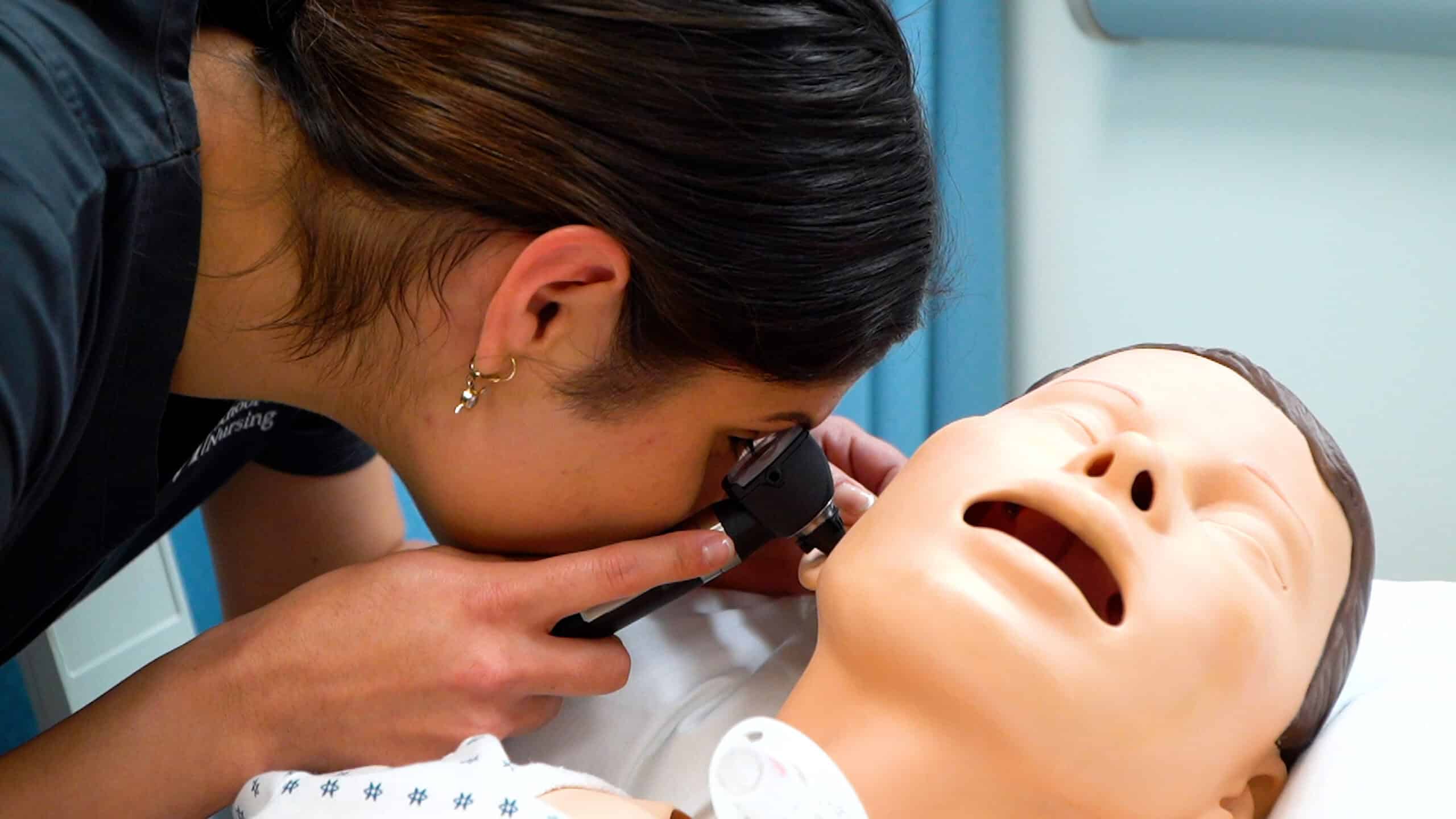 Miramar and Mami ASN nursing student using an instrument looks inside the ear of a patient simulator