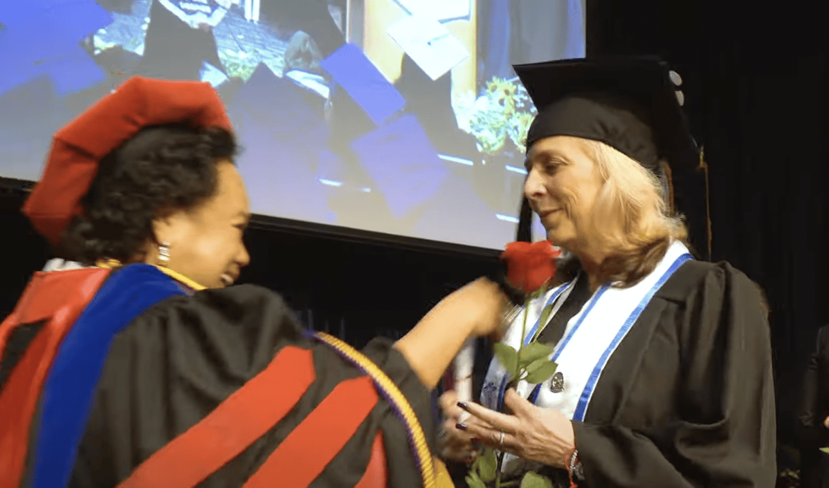 FVI's director of nursing hands a red rose and congratulates an FVI nursing program student at graduation on stage